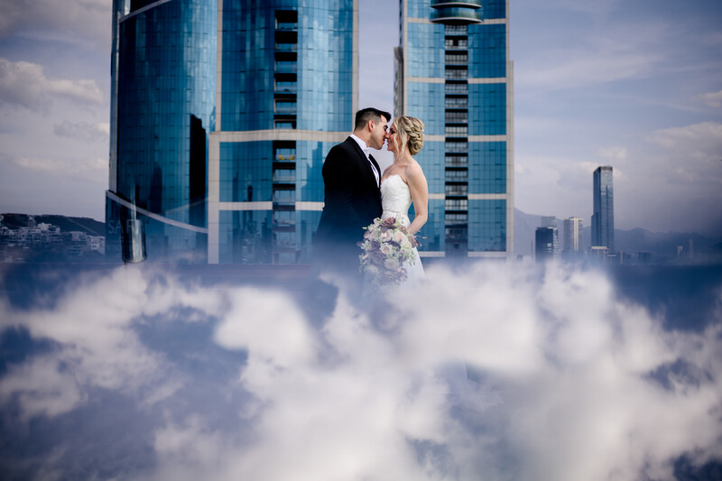 Bride and groom embracing among clouds with city skyscrapers in the background.