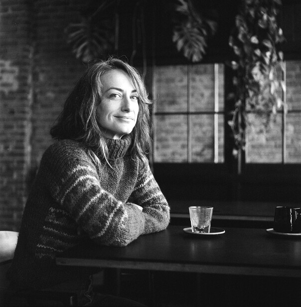 Woman with long hair seated at a table, looking pensively to the side in black and white portrait photography.