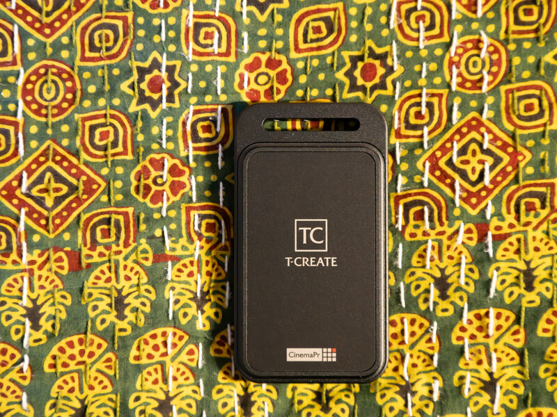 TC CREATE portable power bank on patterned green and gold textile background.
