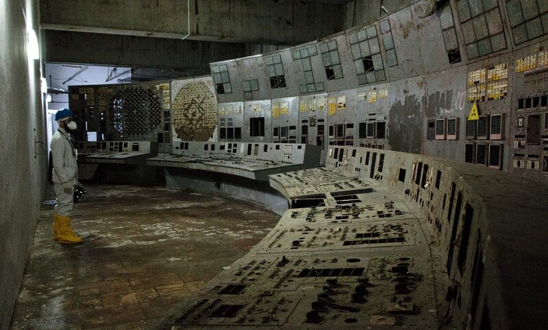 Abandoned nuclear control room with operator at console and walls covered in monitoring panels and gauges.