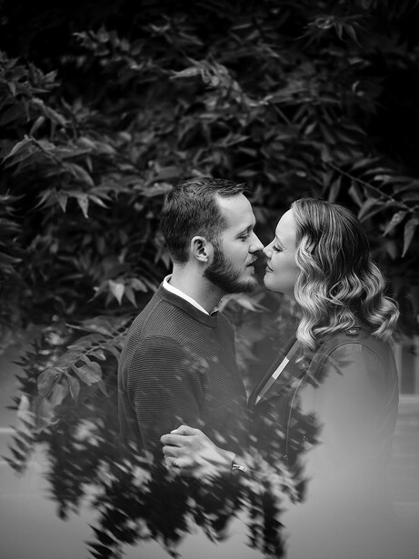 Couple kissing in profile among leafy branches in black and white photography.
