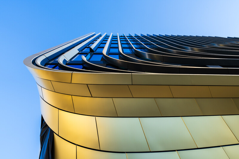 Modern curved building facade with yellow and blue metal panels against clear sky.