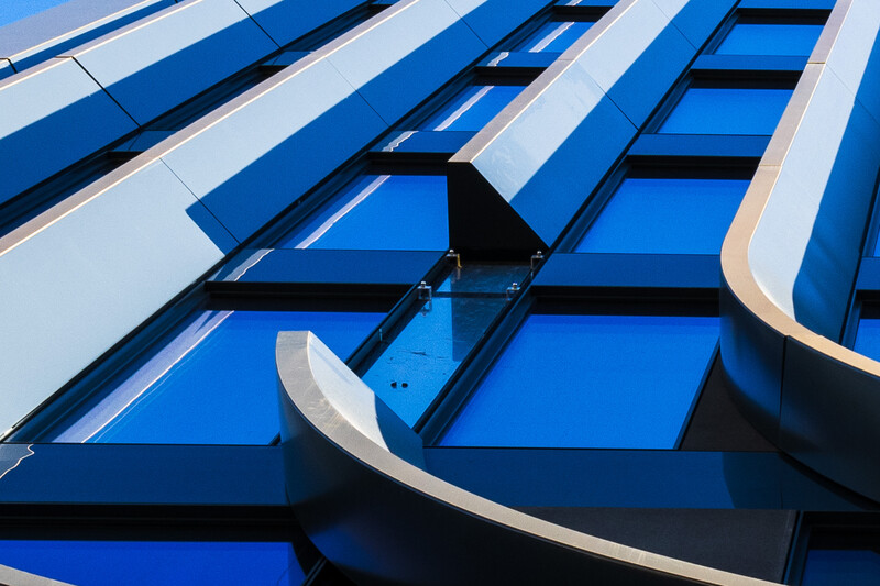 Modern curved architectural facade with blue and white striped panels against a clear sky.