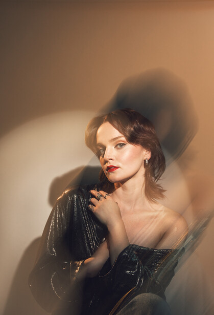 Woman in black leather jacket with dramatic side lighting and shadow projection on wall.