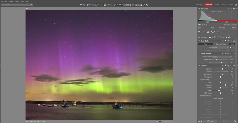 Aurora borealis displaying green and purple bands above a harbor with boats at dusk.