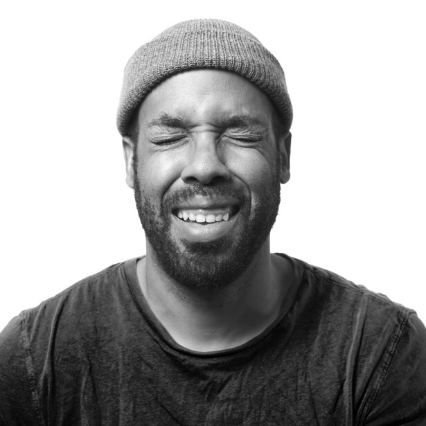 Man with beard wearing gray beanie smiling at camera against white background.