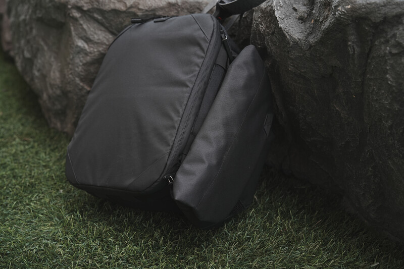 Black camera bag resting against a concrete wall base on grass.