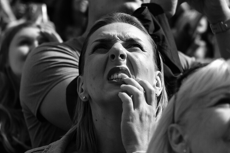 Woman in a crowd with hand to face, looking upward with intense emotion in black and white.