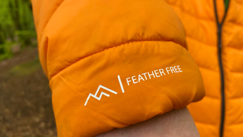 Close-up of bright orange puffy jacket sleeve with white "FEATHER FREE" text and logo.