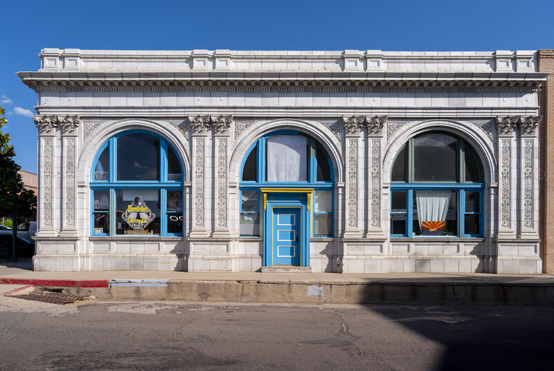 Historic storefront with white stone facade, three arched windows with blue frames, and centered blue door.