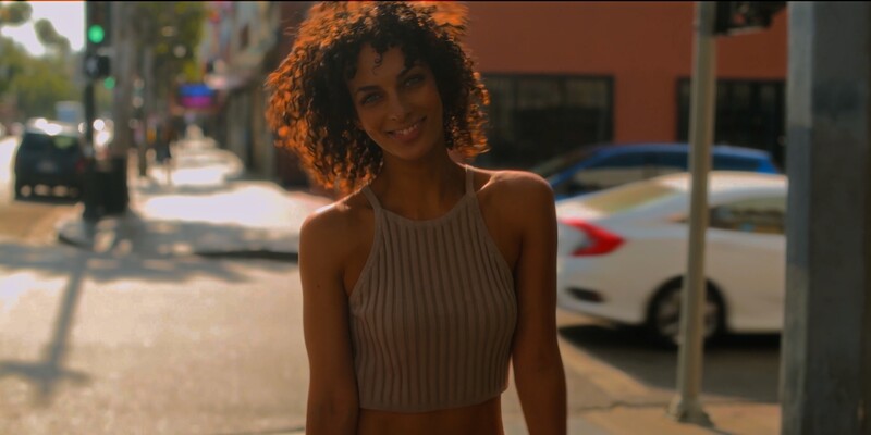 Woman in ribbed halter crop top smiling at camera on urban street during golden hour.