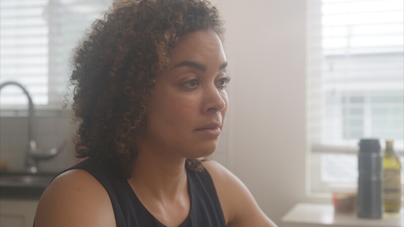 Woman with curly hair looking toward a window in bright, natural light streaming through a kitchen space.