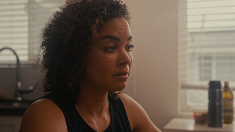 Woman with curly hair looking pensively to the side in a bright, minimalist interior space.