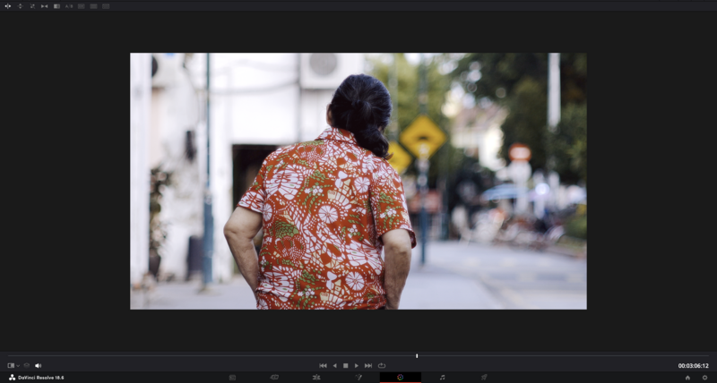 Person wearing a coral floral patterned short-sleeve shirt standing on a street with blurred pedestrians and storefronts in the background.
