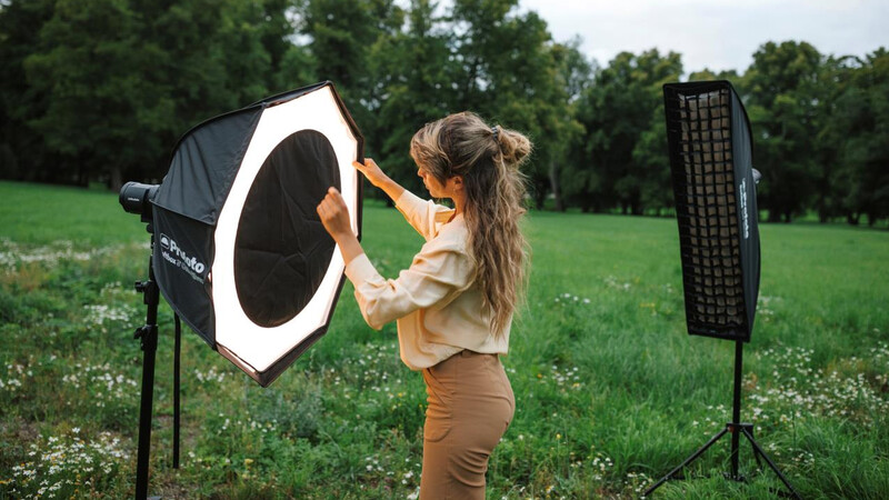 Photographer adjusting a large octagonal softbox while setting up outdoor lighting equipment in a grassy field.