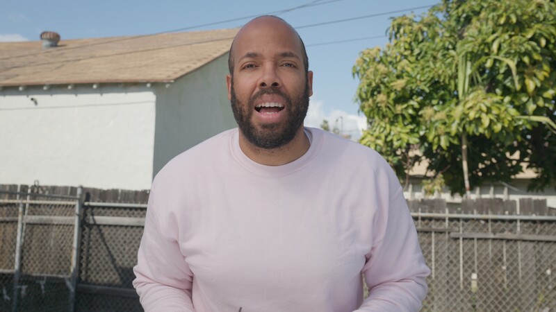 Man in pink long-sleeve shirt smiling at camera in a residential backyard setting.