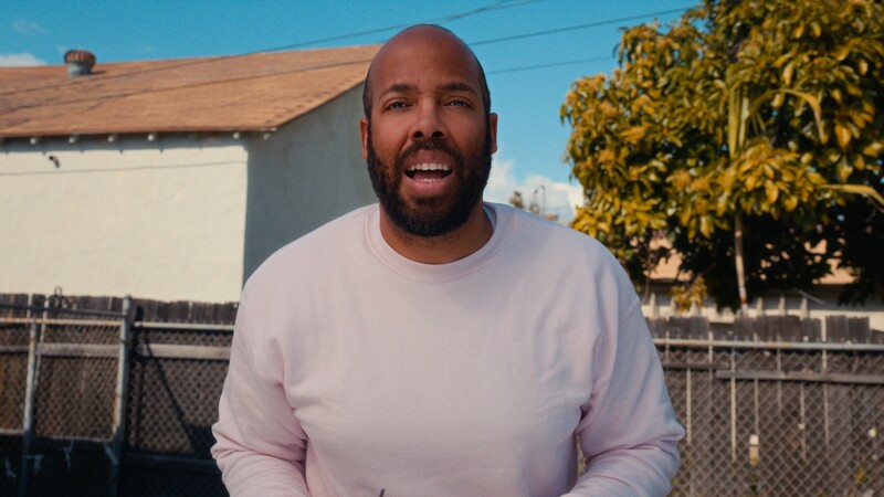 Man in pink long-sleeve shirt smiling at camera in residential backyard.