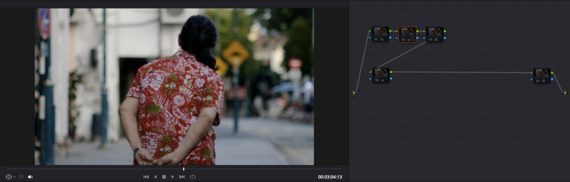 Person wearing red patterned shirt walking away on urban street with blurred pedestrians and storefronts in background.