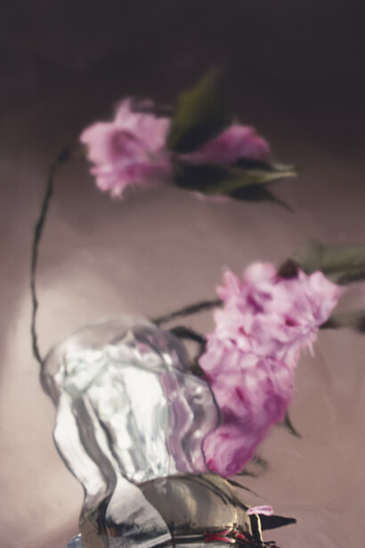 Pink carnations with white tissue paper draped over an overturned bucket against a neutral backdrop.