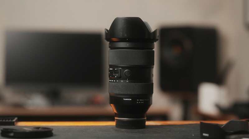 Telephoto zoom lens with hood displayed on orange cable on desk with blurred studio background.