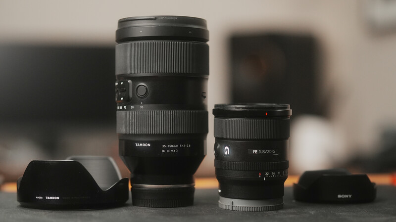 Three camera lenses with hoods arranged on a wooden surface against a blurred studio background.