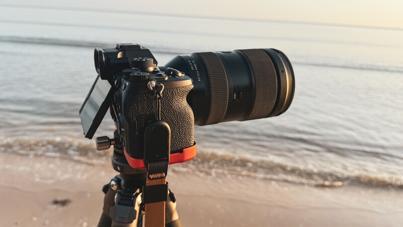 Professional camera with telephoto lens mounted on tripod at beach during golden hour.
