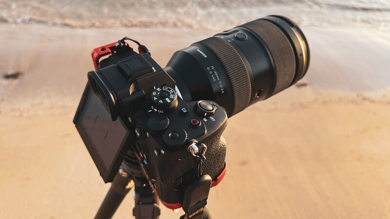 Professional DSLR camera with telephoto lens mounted on tripod at beach location.