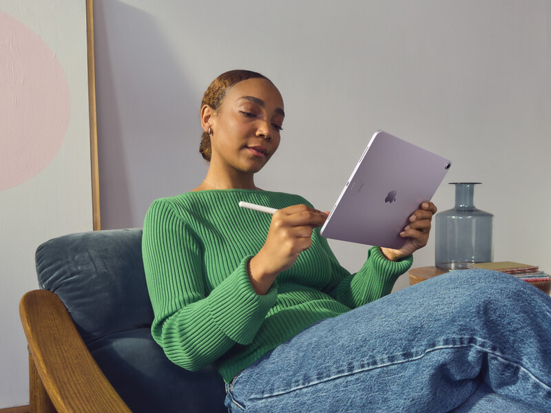 Person in green ribbed sweater holding purple tablet while seated in wooden armchair.