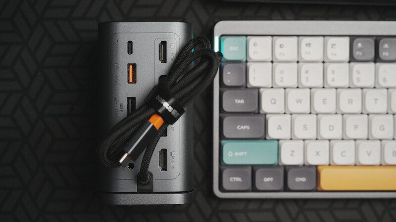 Cylindrical power hub with multiple USB ports next to a mechanical keyboard with colored keycaps on dark textured surface.