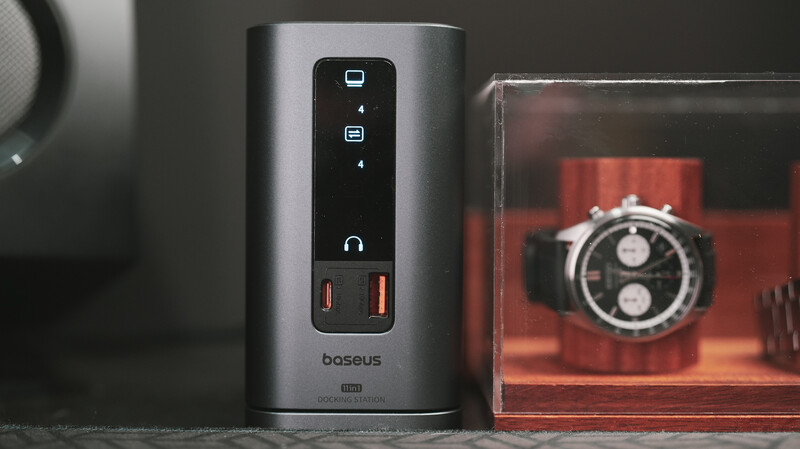 Baseus power bank with dual USB ports and LED indicators displayed next to a vintage chronograph watch in a red shadow box.