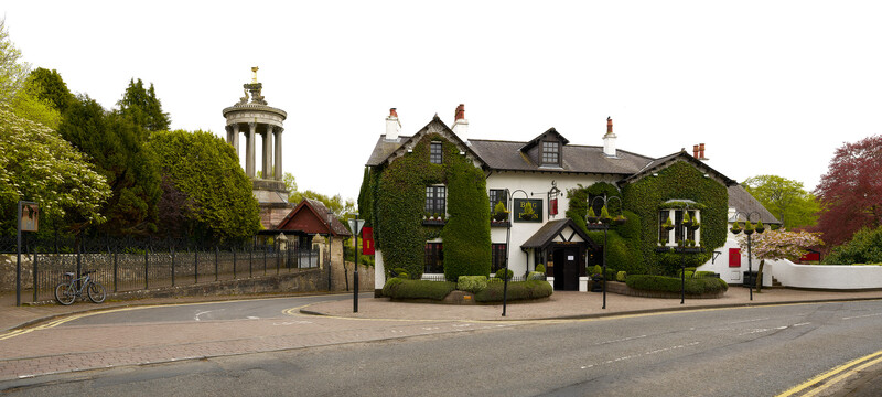 Victorian-era stone buildings with ivy-covered walls beside a classical rotunda structure on a tree-lined street.