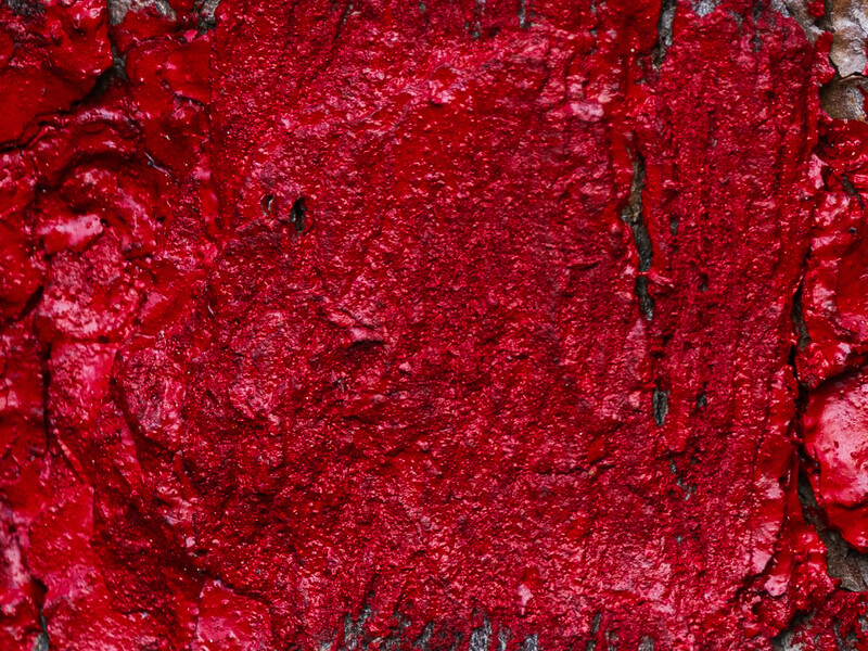 Close-up of vibrant red textured surface with rough, granular patterns and dark cracks.