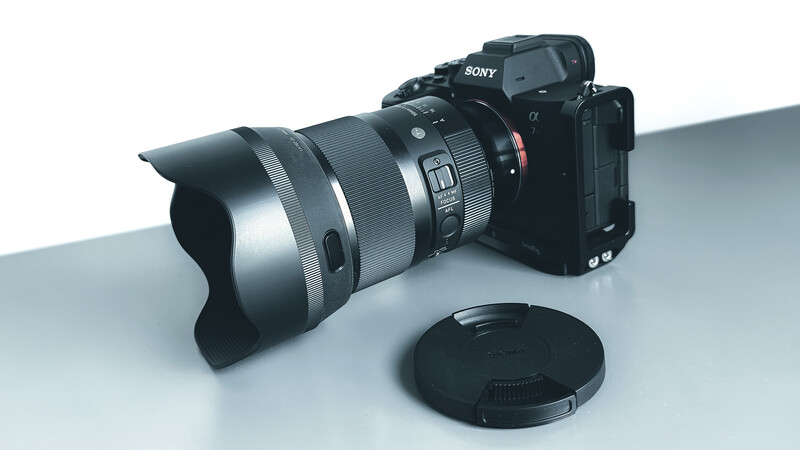 Sony mirrorless camera with silver telephoto lens and lens cap on white surface.