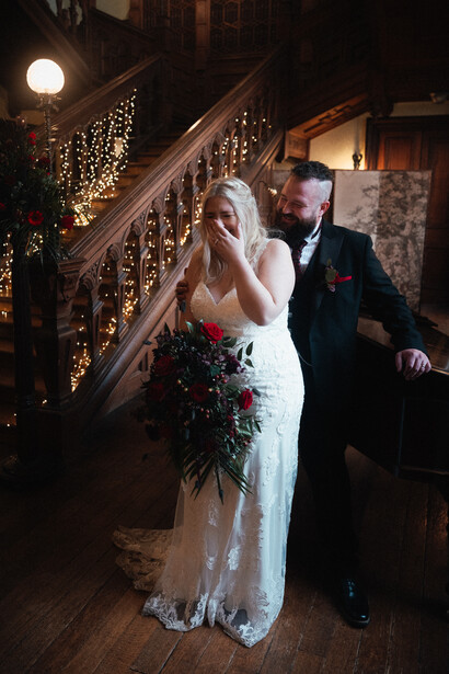 Bride and groom on an ornate staircase decorated with glowing garland lights during evening reception.