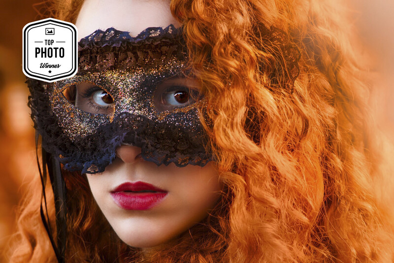 Woman with curly red hair wearing a black glittered masquerade mask with dramatic pink lipstick.