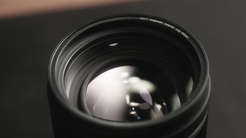 Close-up of camera lens front element showing glass refraction and internal reflections against dark background.