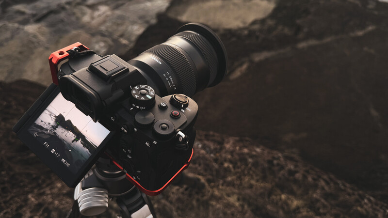 Professional DSLR camera with telephoto lens mounted on tripod against rocky ground.