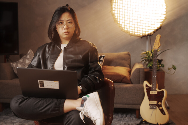 Woman in black leather jacket working on laptop in warm studio lighting setup.