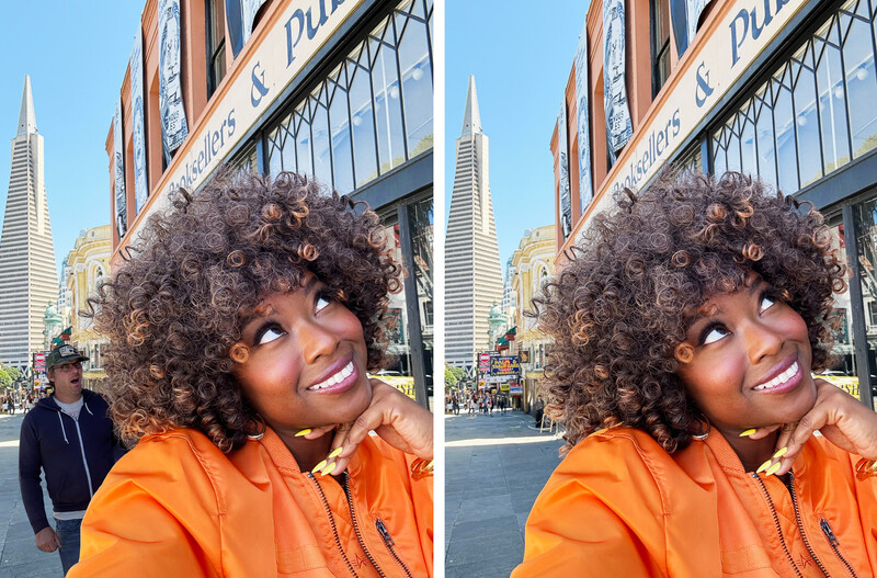 Woman with curly hair in orange hoodie smiling at camera in front of San Francisco architecture.