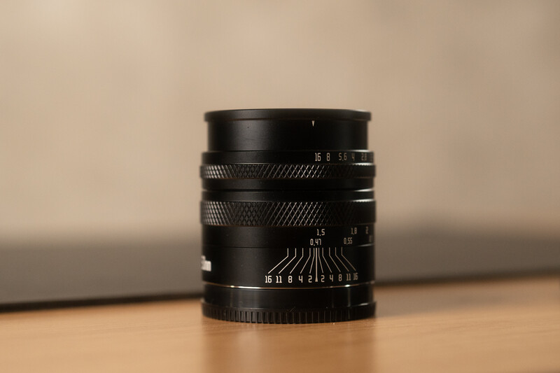 Black manual focus lens with aperture ring and distance scale markings on wooden surface.