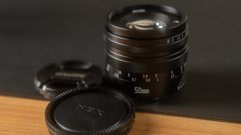 Vintage 50mm lens with rear cap and focusing ring visible on wooden surface.