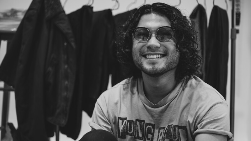 Man wearing sunglasses and graphic t-shirt smiling at camera in black and white portrait.