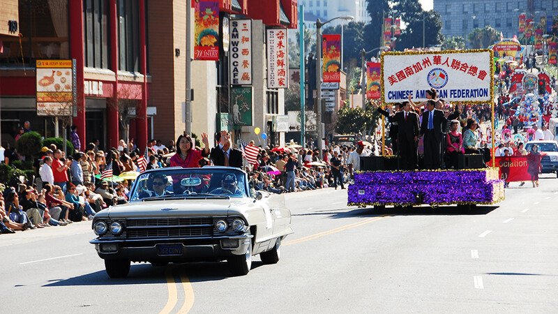 Vintage convertible leading a parade float down a city street lined with spectators.