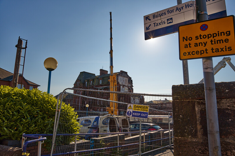 Urban street scene with historic building, taxi rank signage, and protective fencing under clear blue sky.