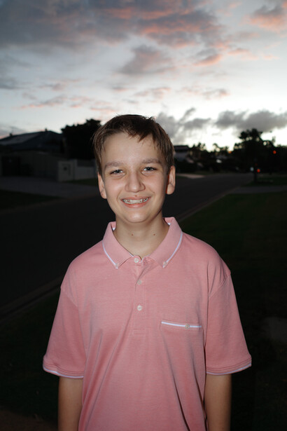 Young boy in pink polo shirt smiling at camera outdoors during golden hour.