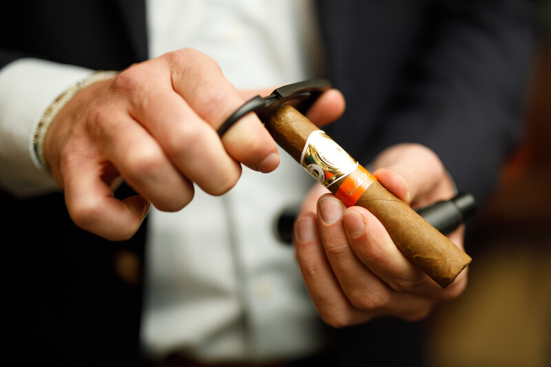Person in formal attire holding a lit cigar between their fingers.