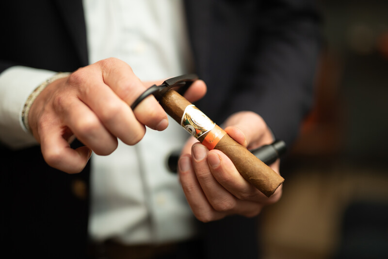 Person in formal attire cutting the end of a cigar with a cutter.