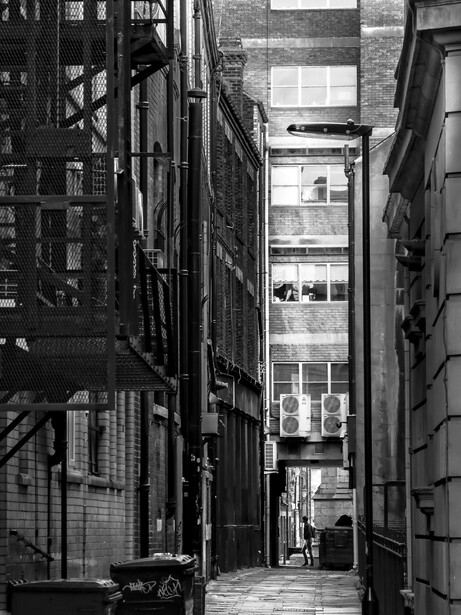 Narrow urban alley between tall buildings converging toward distant street-level perspective.
