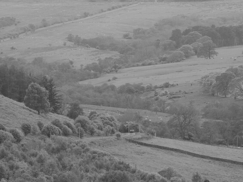 Rolling countryside landscape with layered hills, scattered trees, and a small structure in the middle distance.