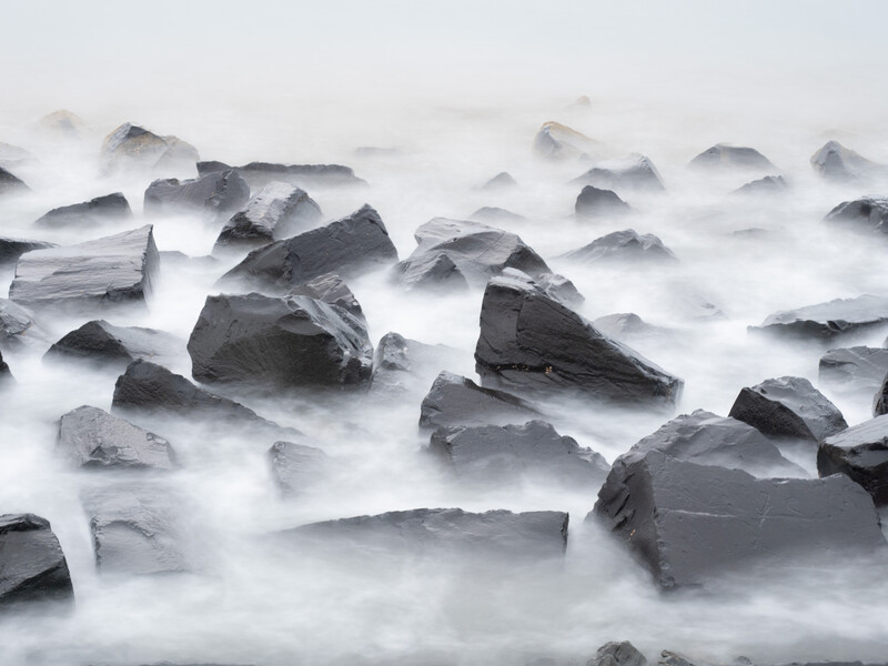 Dark rocks surrounded by silky white ocean waves using long exposure technique.